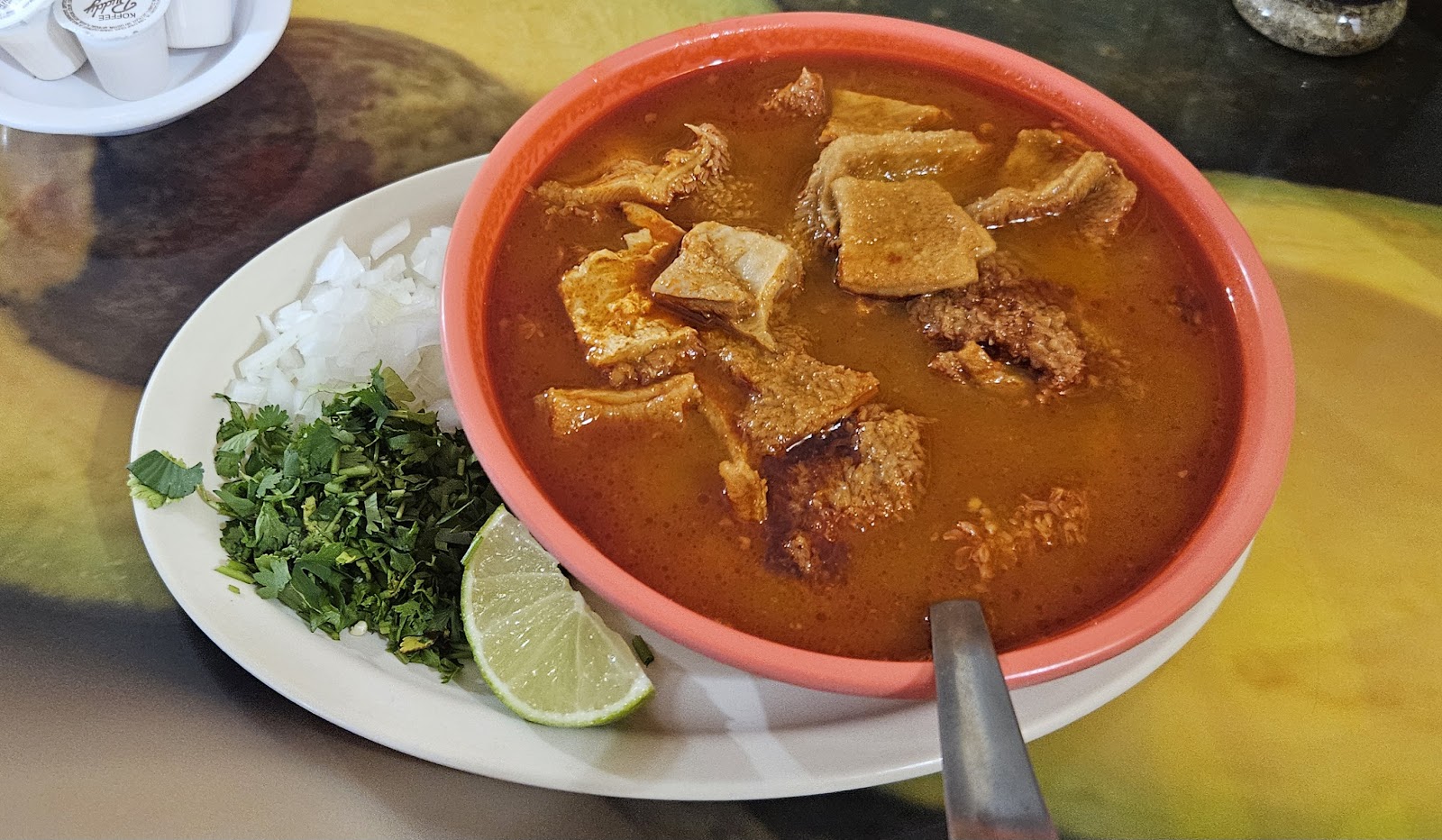 A steaming bowl of homemade menudo with onion, cilantro, and lime at Plaza Arandas